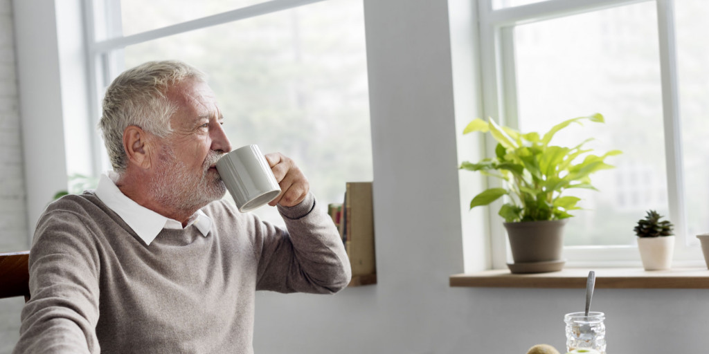 Mann ser ut av vinduet og drikker kaffe. Foto