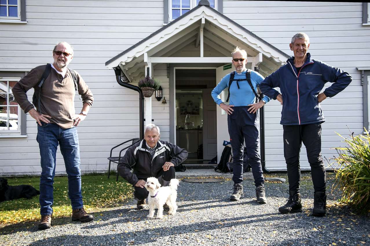 Fire menn og en hund står foran et hus. Foto