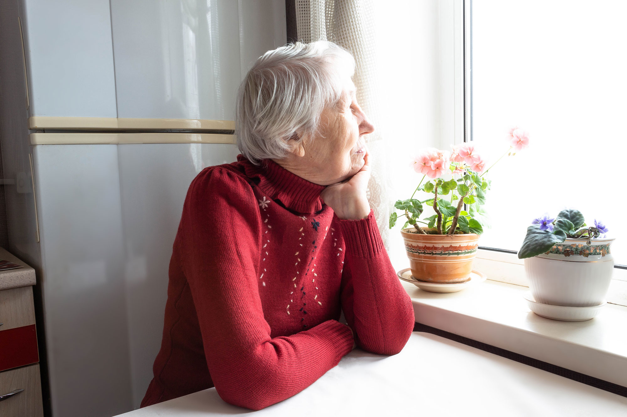 Eldre dame ser ut av vinduet og tenker. Foto