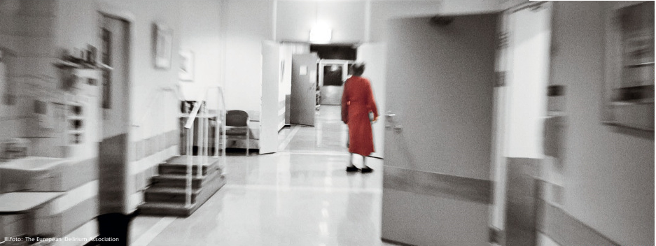 Eldre person i rødt i korridor.