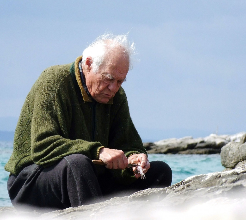 Illustrasjonsfoto: En gammel mann sitter på et svaberg og spikket på en pinne.