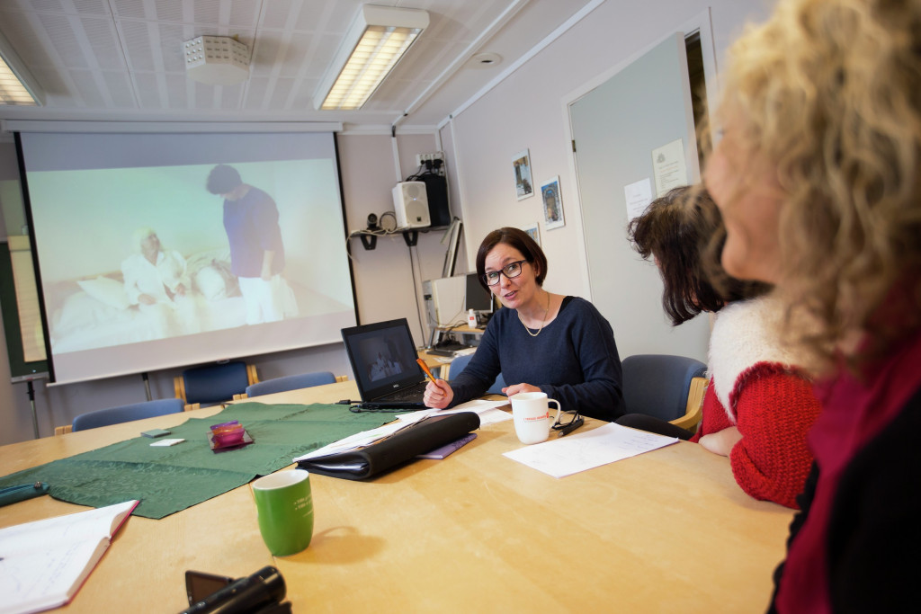 Kvinner rundt et bord med visning av helsearbeid på projektor. Foto.