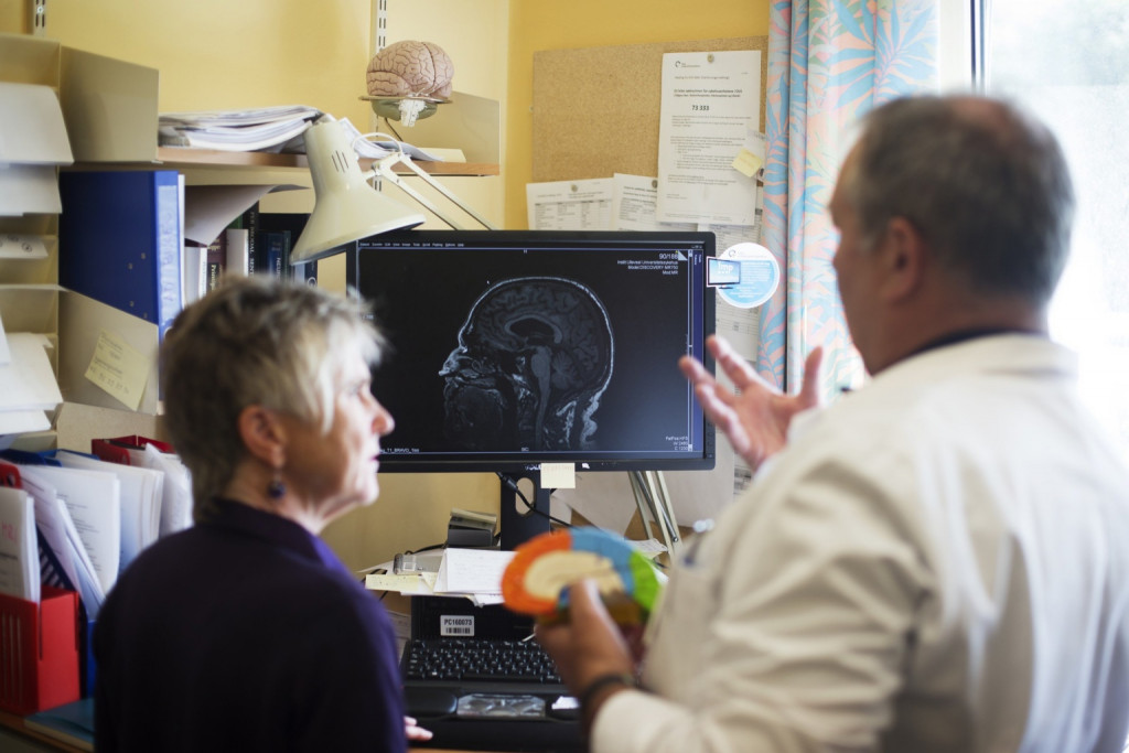 Lege viser eldre kvinne skjerm med røntgenbilde av hjernen. Foto.