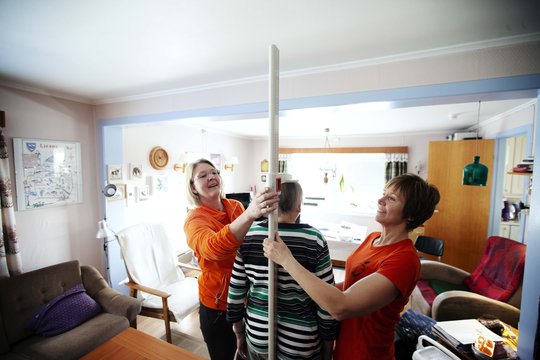 To kvinner måler høyden til eldre kvinne hjemme. Foto