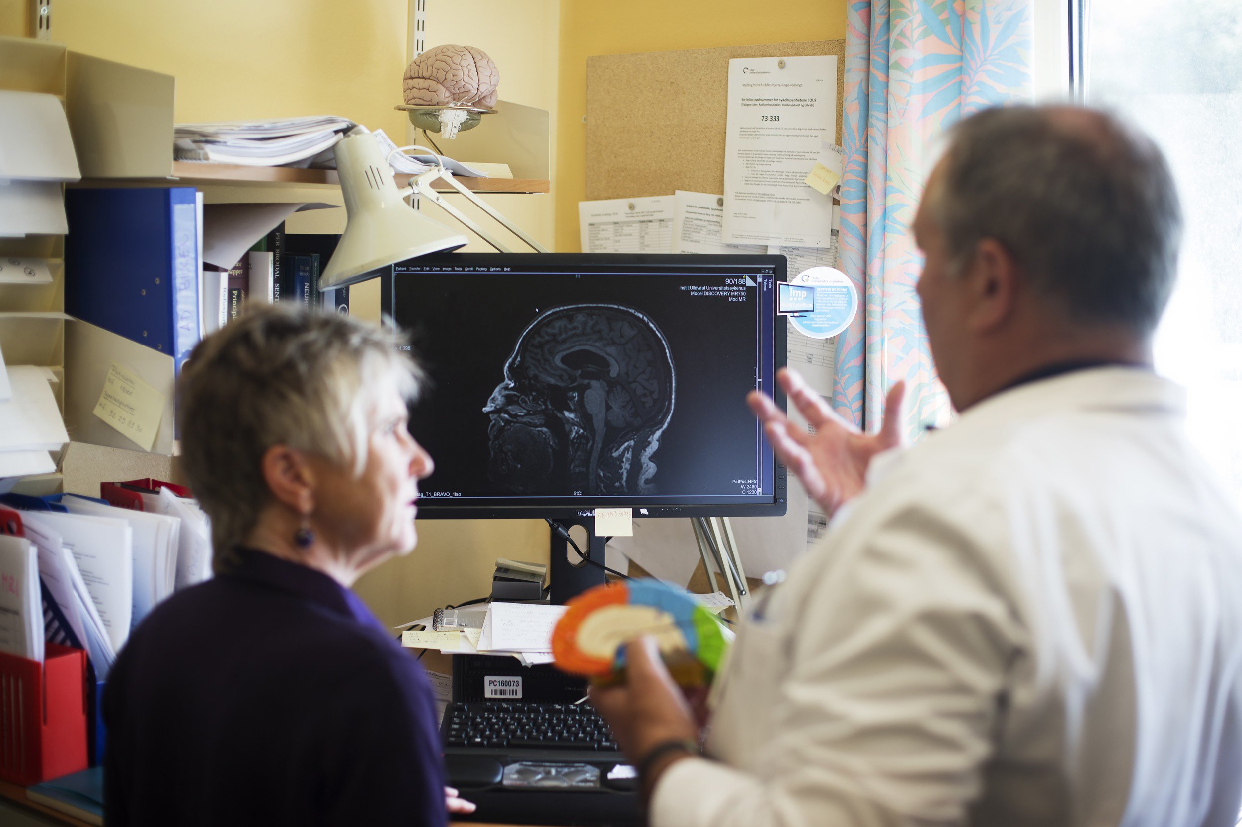 Mannlig helsepersonell og eldre kvinne ser hjerne på skjerm. Foto.