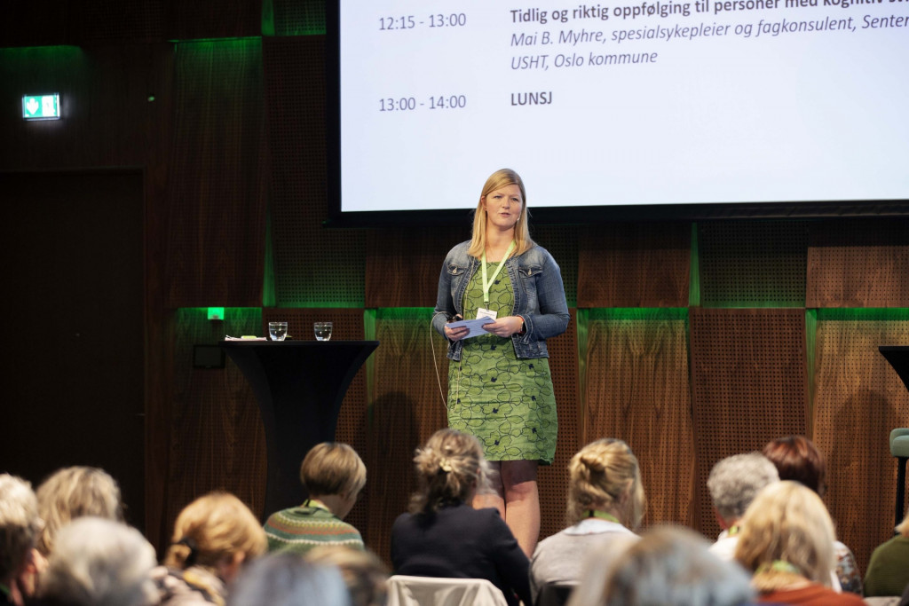 Kvinne står på scene foran forsamling. Foto