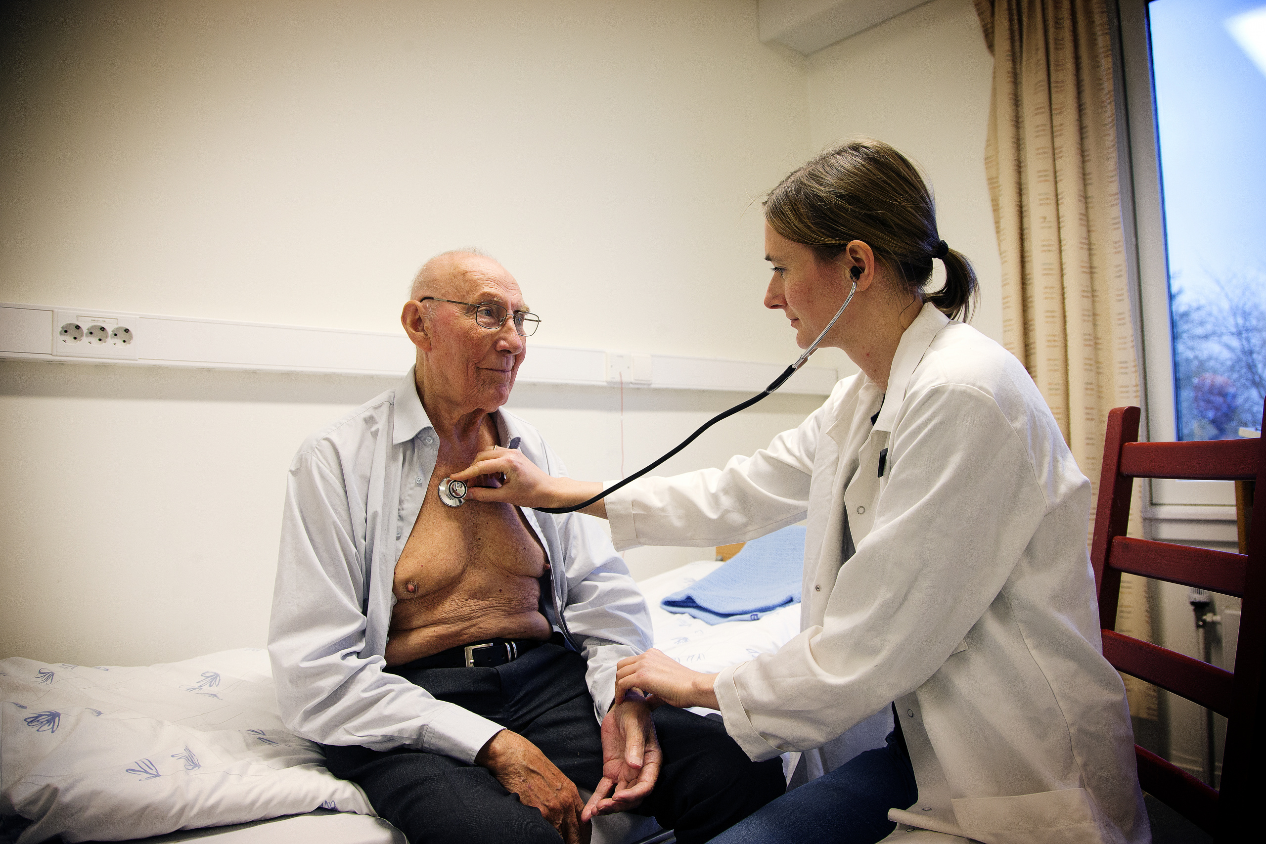 Kvinne lytter til lungene til eldre mann med stetoskop. Foto