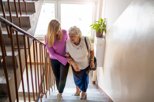 Yngre kvinne støtter eldre kvinne i trappeoppgang. Foto