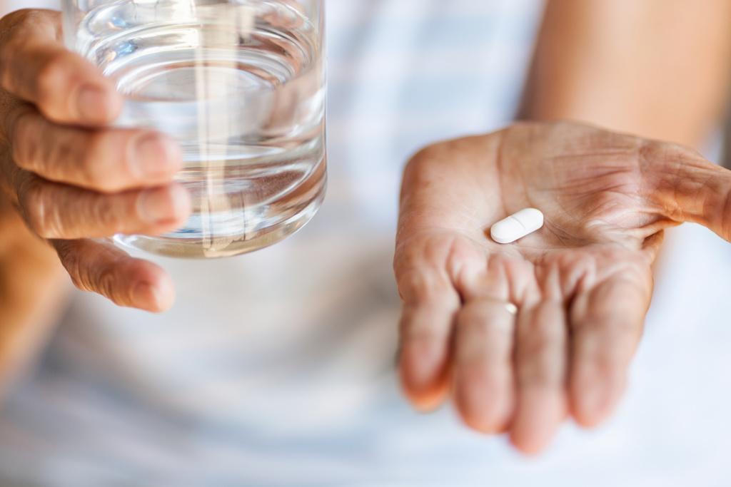 Eldre person holder pille i en hånd og glass med vann i andre.