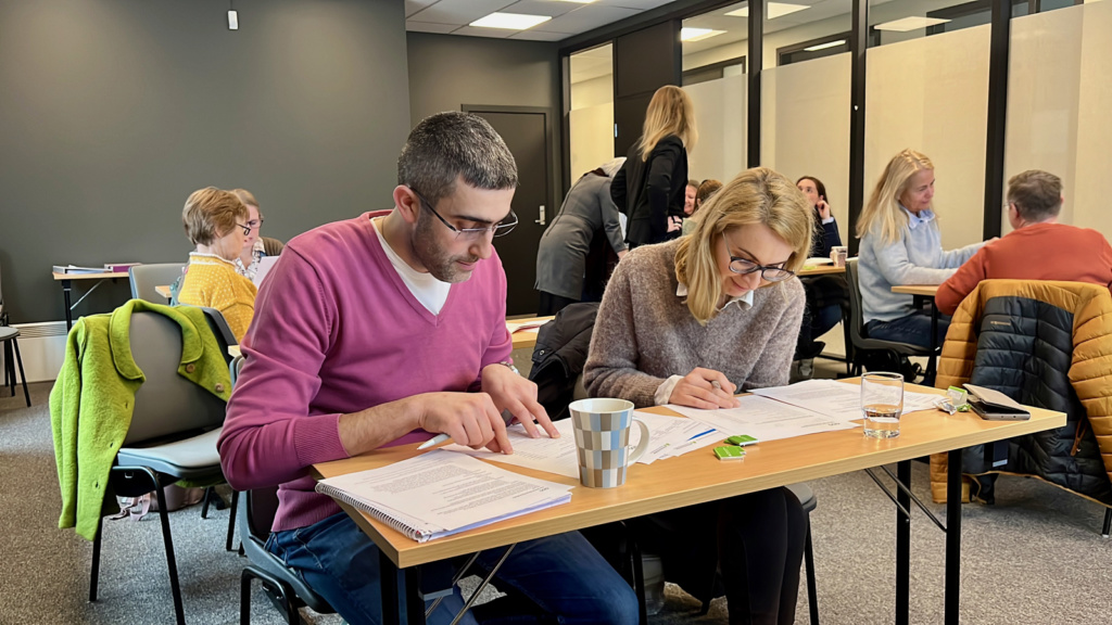 En mann og en kvinne sitter ved pult i klasserom. Foto