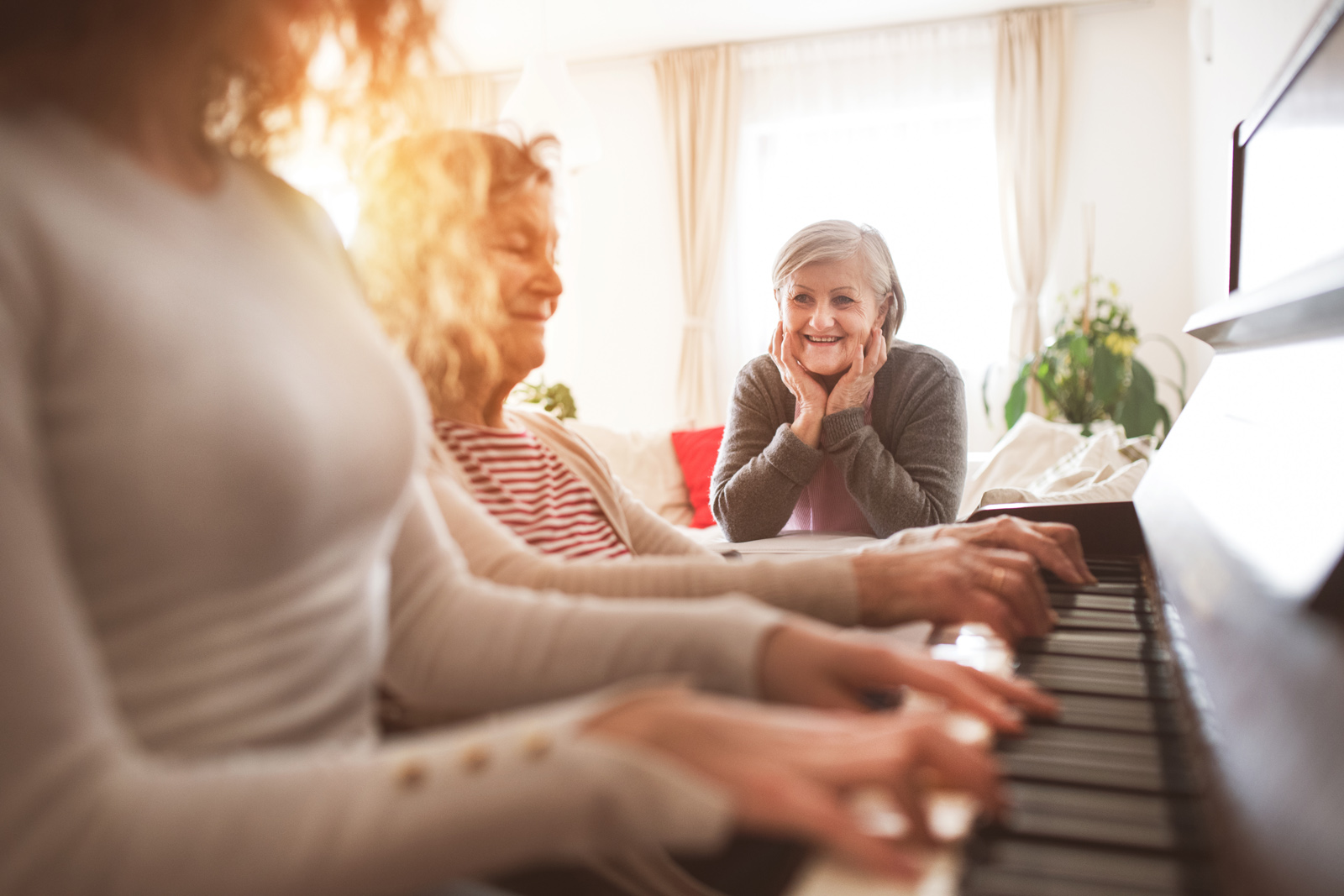 Eldre kvinne hører på pianospill av yngre og eldre kvinne. Foto
