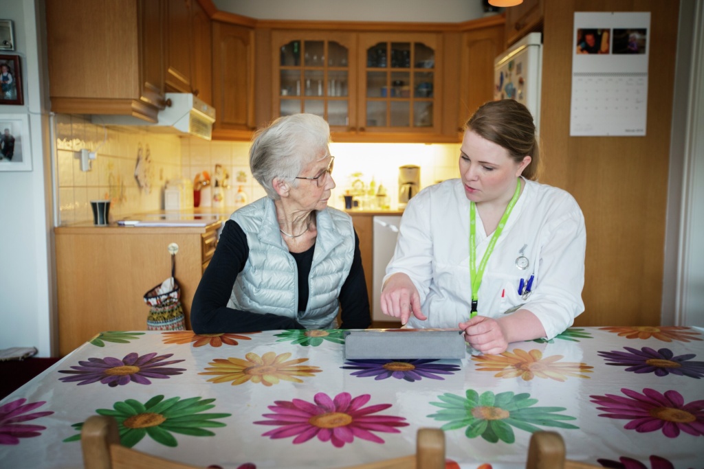 Illustrasjonsfotot av sykepleier som viser elder kvinne hvordan bruke nettbrett.