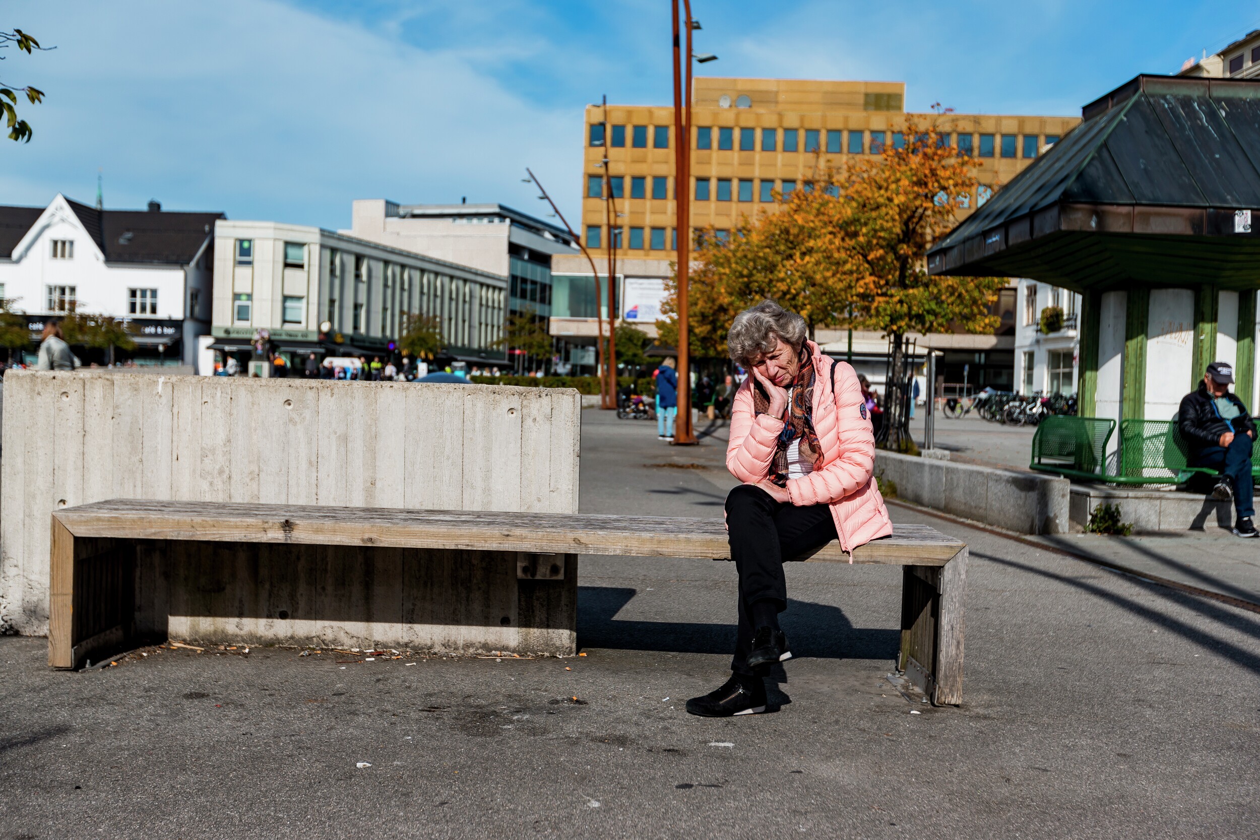 Eldre kvinne sittende på benk i bymiljø.