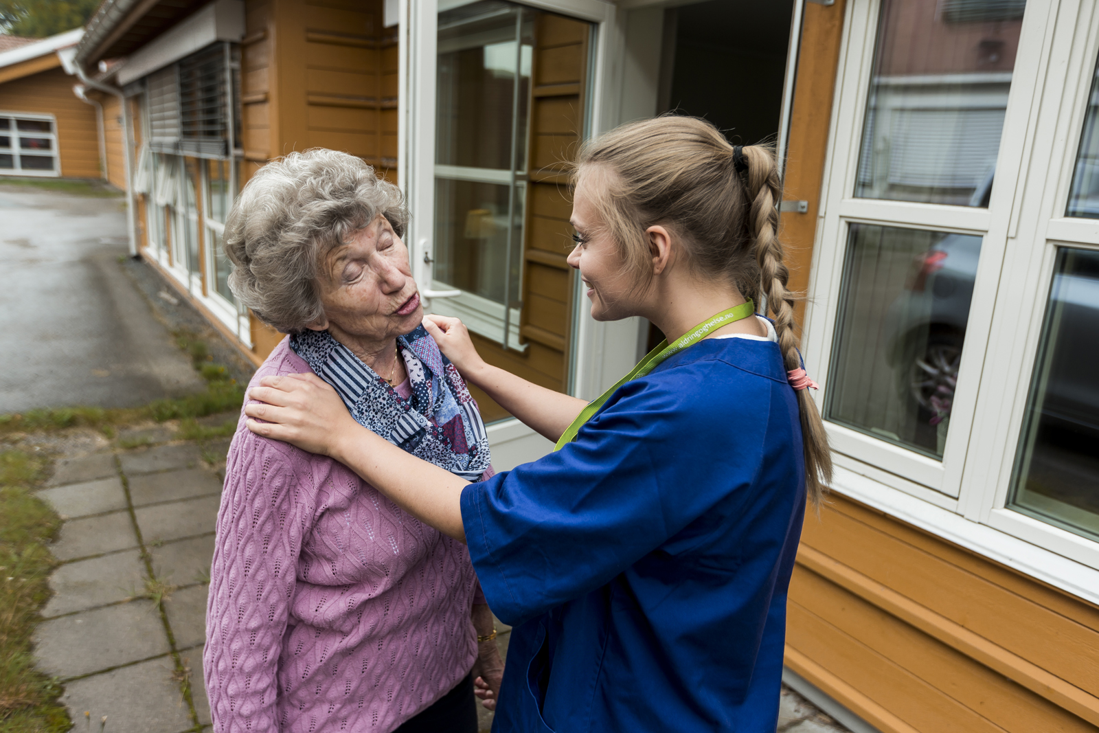 Kvinnelig helsepersonell står overfor eldre kvinne, og holder henne på skuldrene. Foto