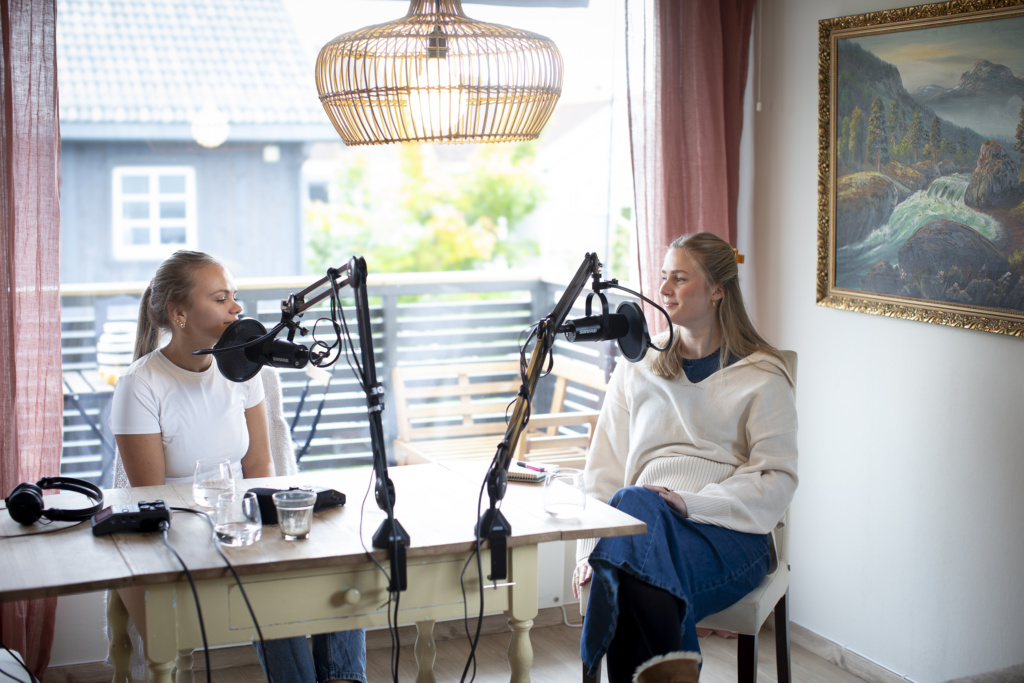To unge kvinner spiller inn podcast hjemme i en stue.