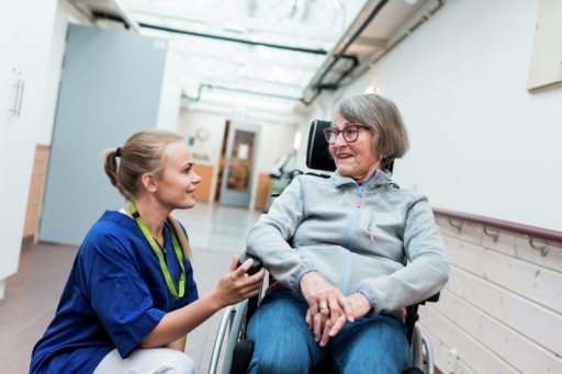 Helsepersonell kommuniserer med eldre kvinne i rullestol. Foto