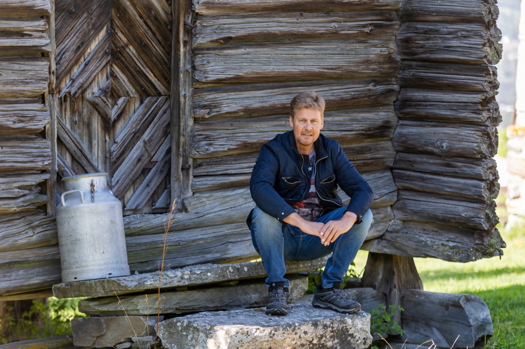 Mann sitter foran stabbur. Foto