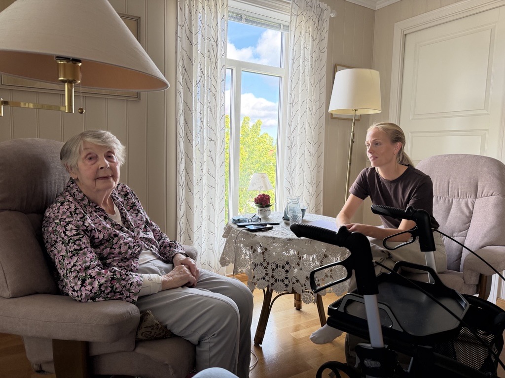 Eldre kvinne i stol og pleier. Foto